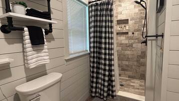 A bathroom with a white toilet, a shower with a checkered curtain, and a window with blinds.