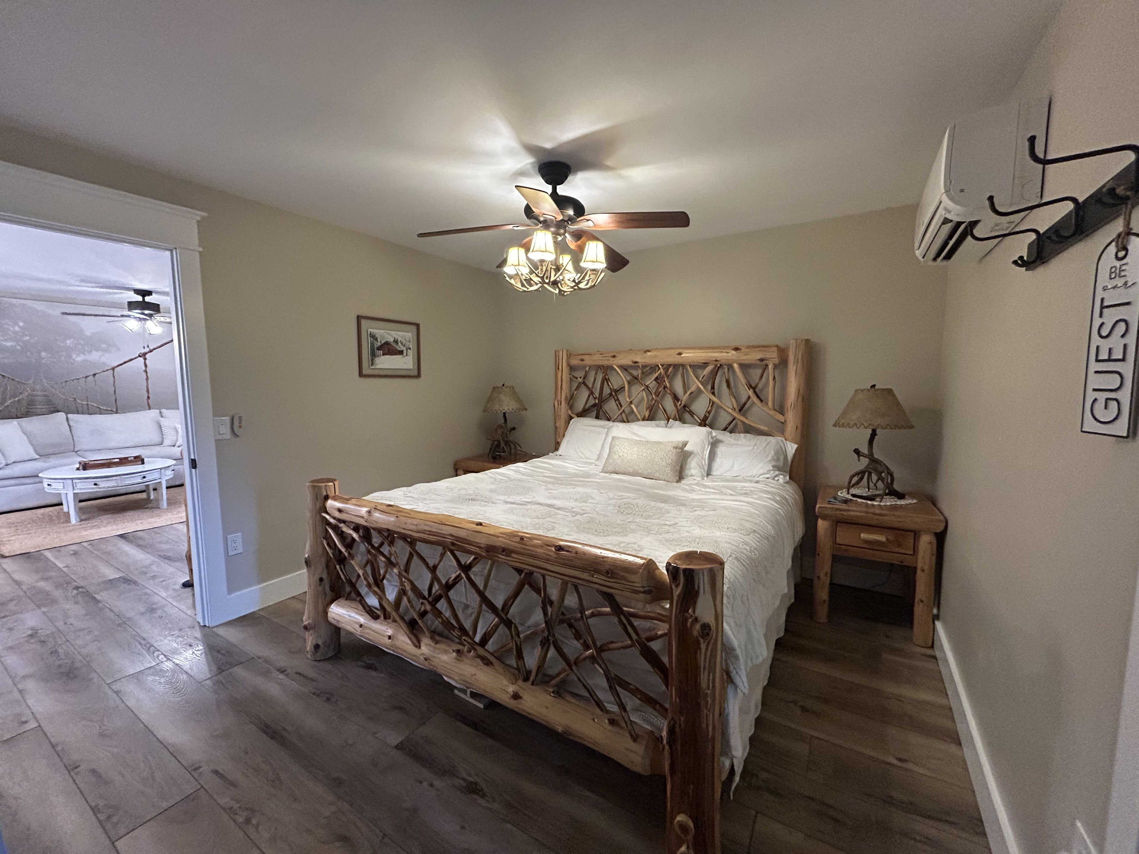 Ein Schlafzimmer mit einem Holzbettgestell, einem Deckenventilator, einem Nachttisch mit Lampe und einer Wand-Klimaanlage.