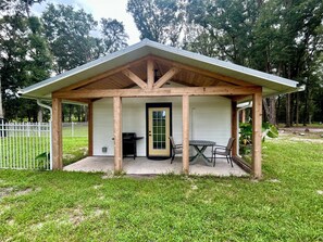 A covered outdoor seating area with a grill, a table, and chairs. - Deer Haven Farmhouse-Cozy 1-Bedroom Cottage in Enchanting High Springs (High Springs)
