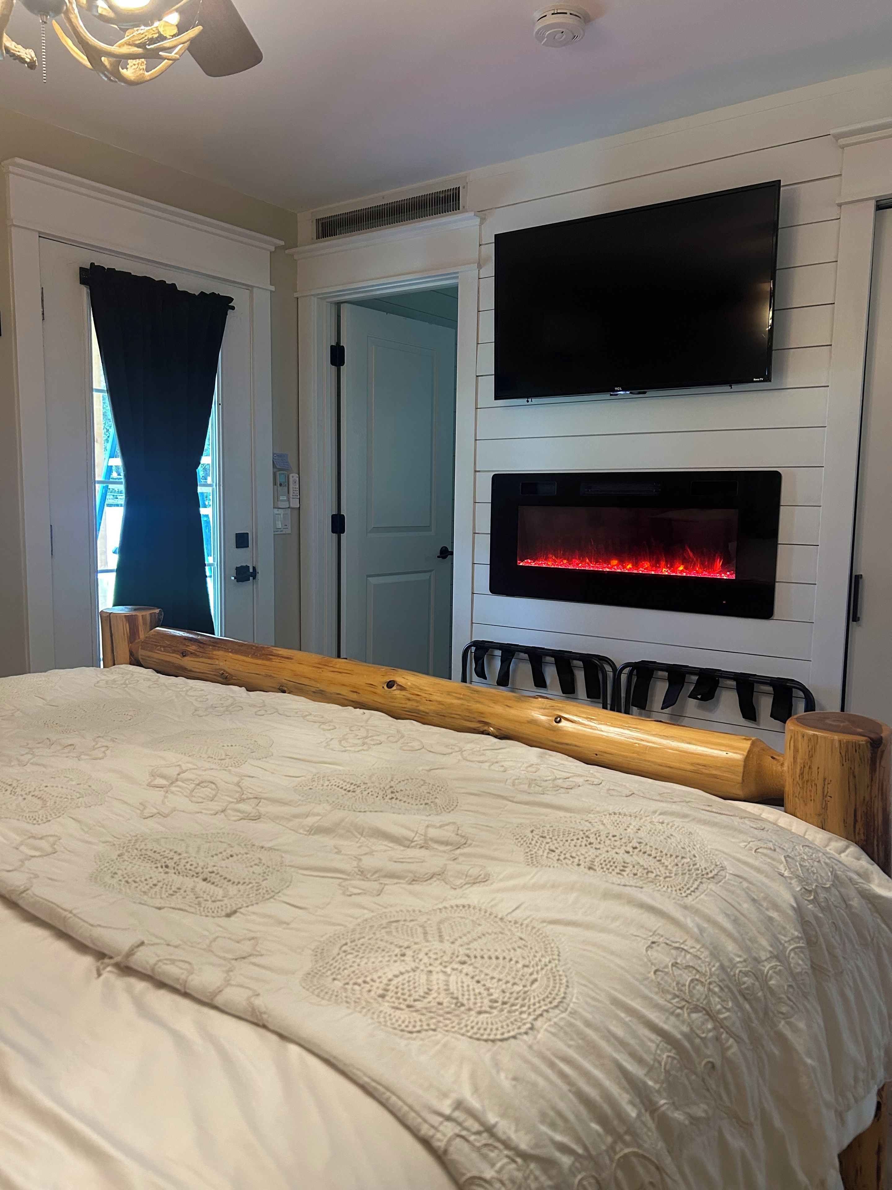 A bedroom with a bed, a television mounted above a fireplace, and a door leading to another room.