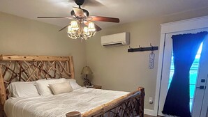 Une chambre à coucher avec une tête de lit en bois, un ventilateur de plafond, un appareil de climatisation et une porte surmontée d’un rideau bleu.