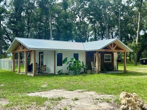 A single-story house with a porch, a small attached garage, and a fenced yard. - Deer Haven Farmhouse-Cozy 1-Bedroom Cottage in Enchanting High Springs (High Springs)