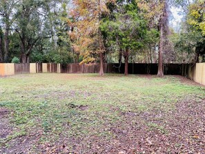 An outdoor area with a wooden fence, trees, and a grassy ground. - Moss Side Cottage | 2BR • Huge Yard • Dogs Welcome (Baton Rouge)