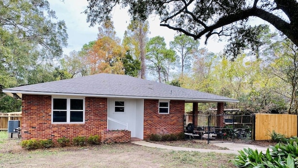 A single-story brick house with a front porch, a small front yard, and a wooden fence. - Moss Side Cottage | 2BR • Huge Yard • Dogs Welcome (Baton Rouge)
