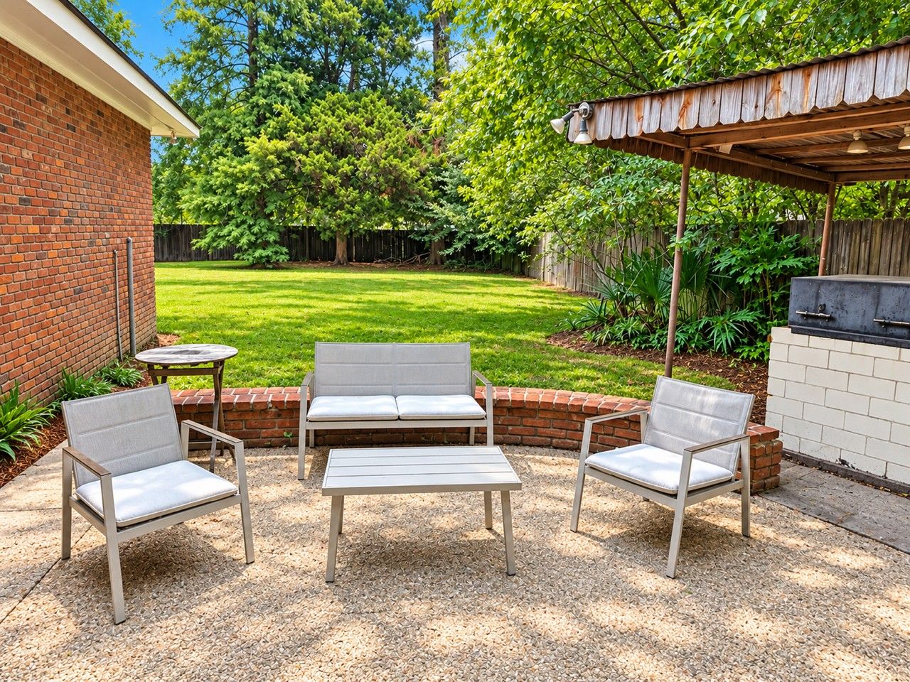 An outdoor patio with a brick wall, a wooden pergola, and a barbecue grill.