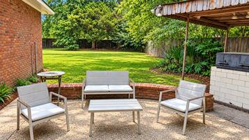 An outdoor patio with a brick wall, a wooden pergola, and a barbecue grill.