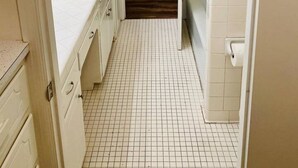 A narrow hallway with a tiled floor, leading to a bathroom with a toilet and sink. - Moss Side Cottage | 2BR • Huge Yard • Dogs Welcome (Baton Rouge)