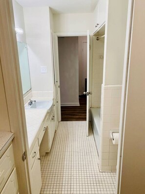 A narrow hallway with a tiled floor, leading to a bathroom with a toilet and sink. - Moss Side Cottage | 2BR • Huge Yard • Dogs Welcome (Baton Rouge)