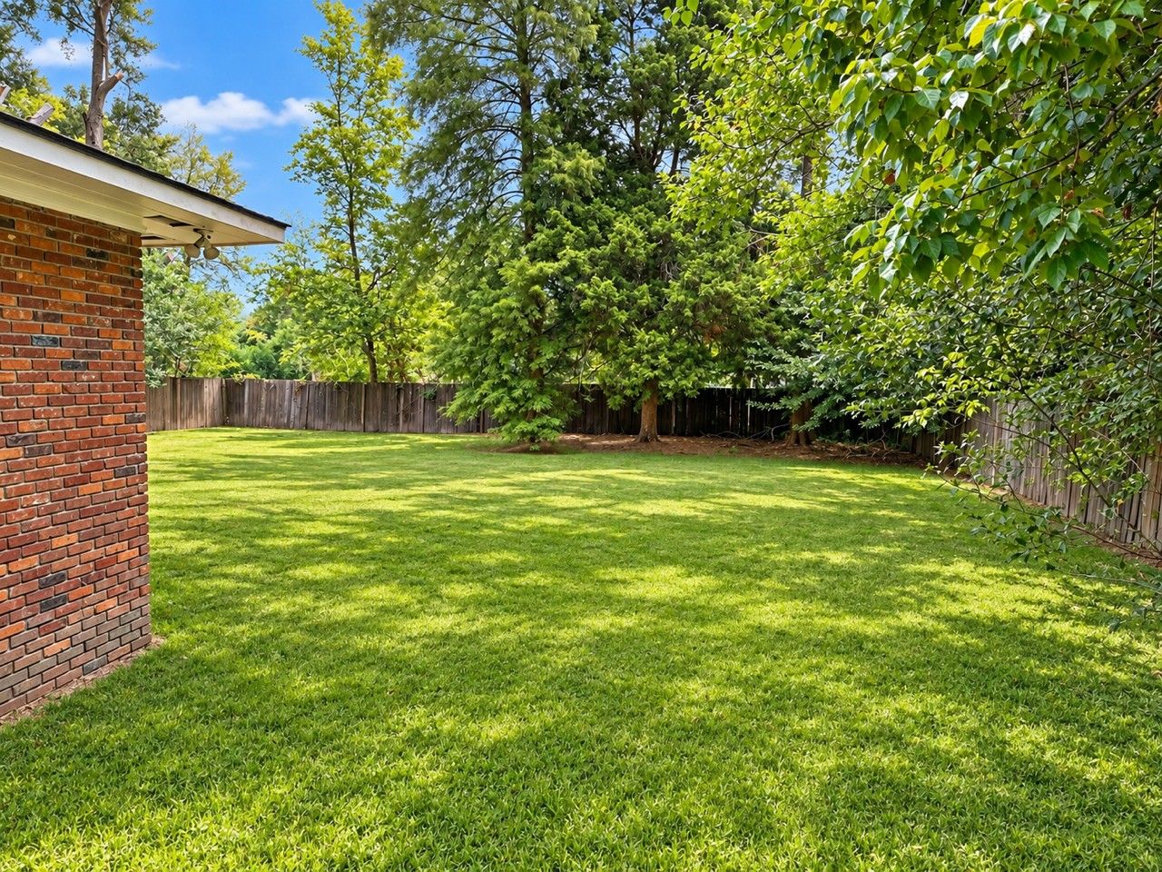 A backyard with a brick wall, a wooden fence, and a grassy lawn.