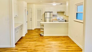 A kitchen with a central island, white cabinetry, and a stainless steel refrigerator. - Moss Side Cottage | 2BR • Huge Yard • Dogs Welcome (Baton Rouge)