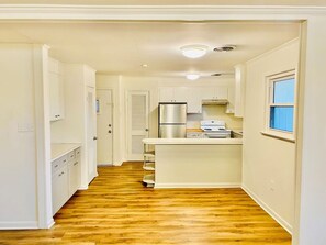 A kitchen with a central island, white cabinetry, and a stainless steel refrigerator. - Moss Side Cottage | 2BR • Huge Yard • Dogs Welcome (Baton Rouge)