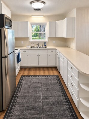Una cocina moderna con armarios blancos, un refrigerador de acero inoxidable, horno empotrado y ventana sobre el fregadero.
