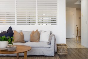A living room with a grey sofa, a round wooden coffee table, a potted plant, and a woven basket. - Ocea Coastal Luxe at Chevron (Surfers Paradise)