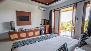 Quarto de hotel com cama, escrivaninha, cadeira, televisão e porta de correr para uma varanda.