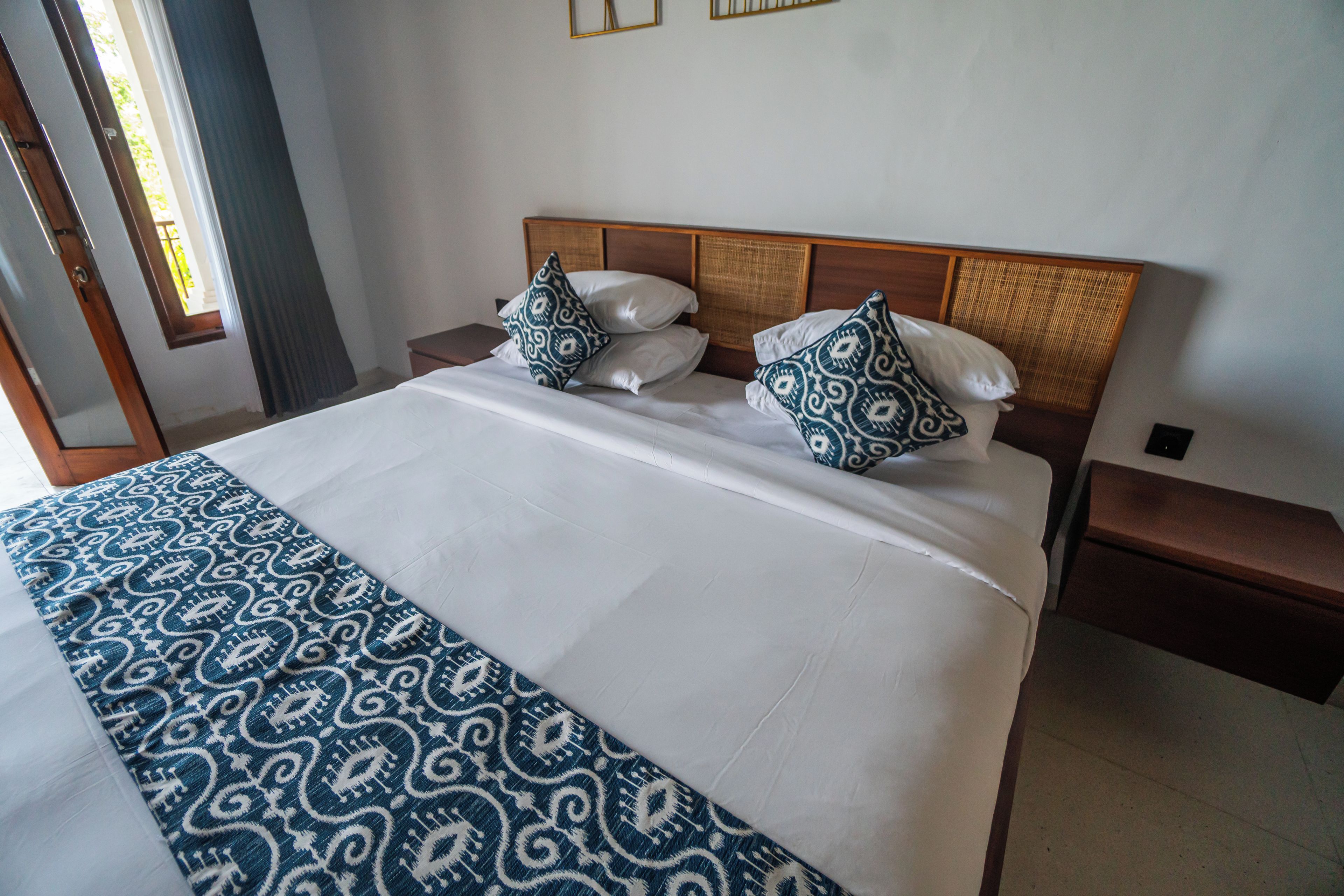 A hotel room with a bed, two nightstands, a window with curtains, and a door.