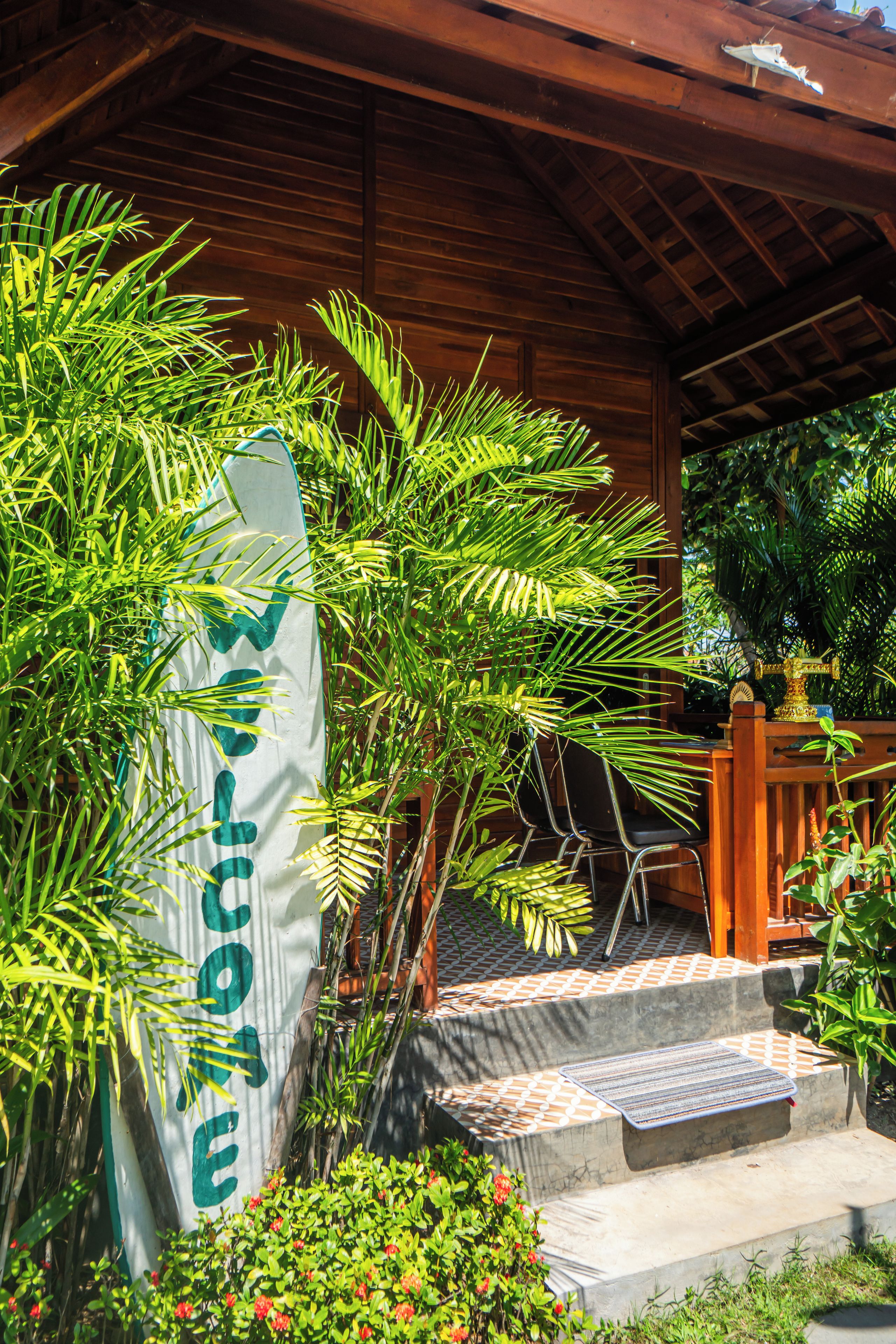 A wooden structure with a signboard, surrounded by lush greenery and a tiled floor.