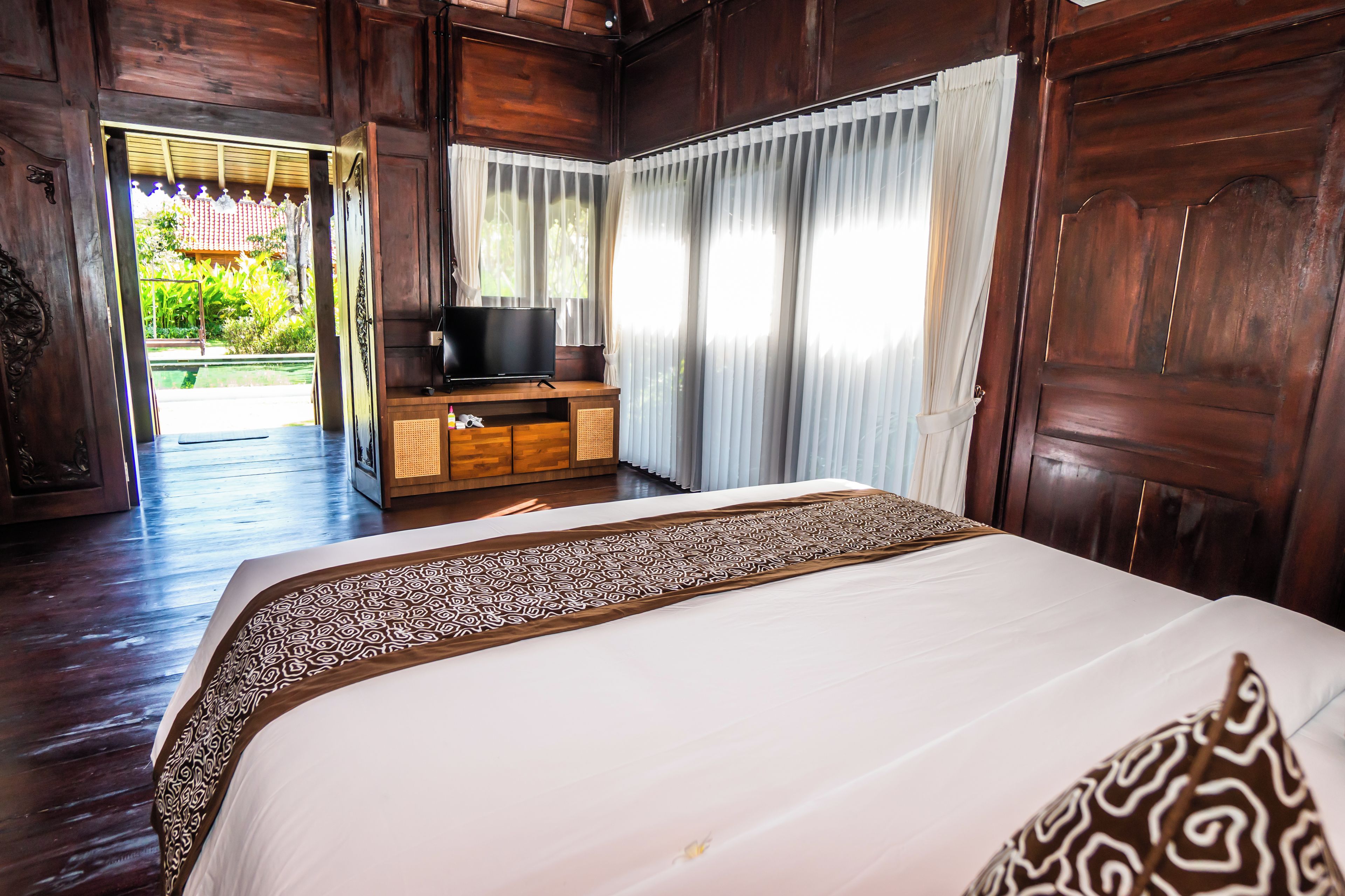 A wooden room with a bed, a television, and a window with curtains.