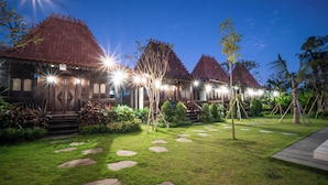 Um edifício tradicional com telhado de azulejos, rodeado por um jardim bem cuidado, com caminhos de pedra e plantas tropicais.