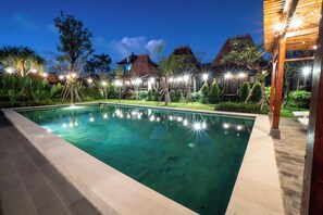 Una piscina con superficie de agua cristalina azul, rodeada por un jardín bien cuidado con diversas plantas y árboles.
