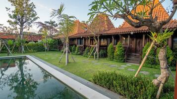 Una casa de madera tradicional con techo de tejas, rodeada de un jardín cuidado con piscina.