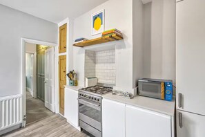 A modern kitchen with white cabinetry, a gas stove, a microwave, and a built-in oven. - Modern South West London Flat Near Richmond Park - Pass the Keys (London)