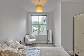 Quarto com cama, cadeira, guarda-roupa, janela e luminária pendente.