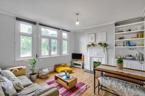A modern living room with a sofa set, a coffee table, a fireplace, and a bookshelf. - Modern South West London Flat Near Richmond Park - Pass the Keys (London)