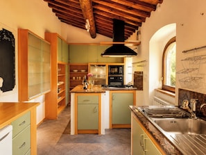 A kitchen with wooden cabinets, a central island, a stove, and a window. - Stone farmhouse in the Umbrian hill countryside (Montone)
