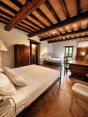 A bedroom with a large bed, a wooden wardrobe, a desk with a chair, and a window.