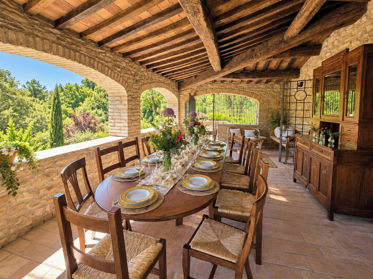 A stone-walled outdoor dining area with a wooden table set for six, surrounded by wicker chairs.