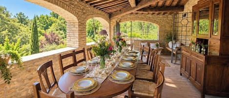 A stone-walled outdoor dining area with a wooden table set for six, surrounded by wicker chairs.