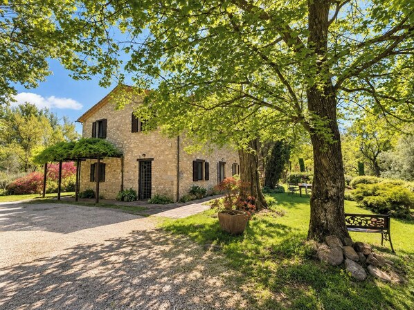 A stone house with a covered porch, a gravel driveway, and a well-maintained garden with a bench.