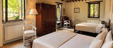 Een slaapkamer met een houten plafond, een bed met een witte dekbedovertrek, een stoel, een kledingkast en een raam met uitzicht op groen.