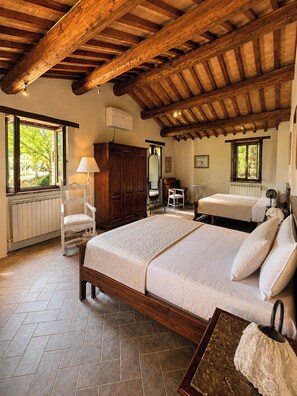 A bedroom with a wooden ceiling, a bed with a white bedspread, a chair, a wardrobe, and a window with a view of greenery. - Stone farmhouse in the Umbrian hill countryside (Montone)