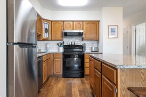 A kitchen with wooden cabinets, stainless steel appliances, and a granite countertop. - Ocean Reef 5-A1 | Oceanfront Condo (Emerald Isle)