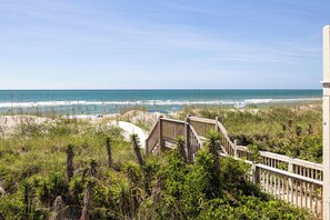 A beach view with a wooden boardwalk leading to the shore, surrounded by dense vegetation. - Ocean Reef 5-A1 | Oceanfront Condo (Emerald Isle)