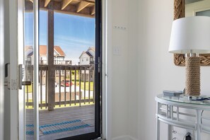 A room with a sliding glass door leading to a balcony, a white wall, a round table with a rope base, and a white lamp. - Ocean Reef 5-A1 | Oceanfront Condo (Emerald Isle)