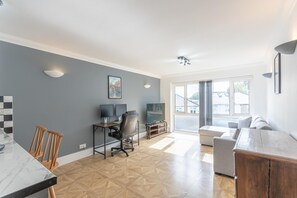 A modern living room with a dining area, a workspace with computers, and a large window with a view of the outside. - Modern City Centre Apartment | Sleeps 4 | Parking - Pass the Keys (Chelmsford)