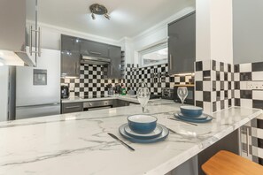 A modern kitchen with a marble countertop, checkered backsplash, and stainless steel appliances. - Modern City Centre Apartment | Sleeps 4 | Parking - Pass the Keys (Chelmsford)
