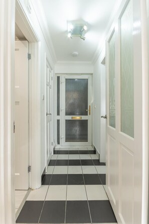 A hallway with a black and white tiled floor, white walls, and a door with a glass panel. - Modern City Centre Apartment | Sleeps 4 | Parking - Pass the Keys (Chelmsford)