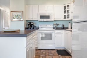 A kitchen with white cabinets, a microwave, a stove, and a coffee maker. - Pier Pointe 4B1 | Oceanfront 2 BR Condo (Emerald Isle)