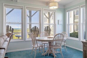 A room with a round table and chairs, large windows, a blue carpet, and a view of the beach. - Pier Pointe 4B1 | Oceanfront 2 BR Condo (Emerald Isle)