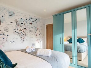 Ein Schlafzimmer mit einem großen Bett, einem Kleiderschrank mit Spiegel sowie einer Wand mit einer Karte und verschiedenen Illustrationen.