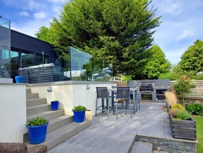 Eine moderne Terrassenanlage im Freien mit Glasgeländer, Sitzgelegenheiten und Grillbereich.