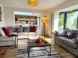 Ein modernes Wohnzimmer mit einer Couch, einem Couchtisch und Blick auf eine Küche und einen Balkon.