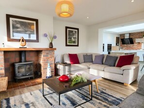 Ein modernes Wohnzimmer mit Kamin, Sofa und einer Küche im Hintergrund.