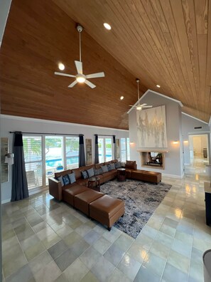A spacious living room with a large sectional sofa, a fireplace, and a view of a swimming pool through large windows. - SlipAway TreasureCay (Treasure Cay)