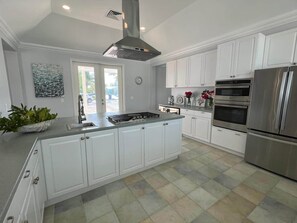 A modern kitchen with white cabinetry, a central island, stainless steel appliances, and a view through the glass door. - SlipAway TreasureCay (Treasure Cay)