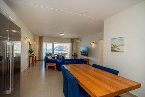 Habitació d'hotel moderna amb taula de dinar de fusta, cadires blava amb tapisseria, un finestral amb vista a una muntanya i un televisor de pantalla plana penjat a la paret.