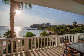 Een balkon met uitzicht op zee, palmbomen en een gebouw op de achtergrond.